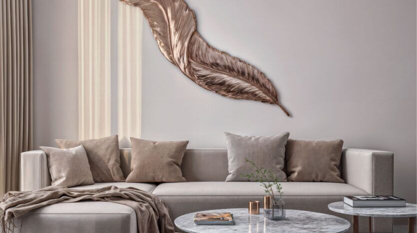 Un salon moderne avec un canapé sectionnel beige, des coussins neutres, une couverture douillette, des tables basses rondes en marbre avec des livres et une plante, et de l'art mural en plumes métalliques sur un mur clair - parfait pour les espaces contemporains comme Butterfly Towers Arjan.