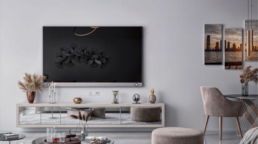 Salon moderne de Butterfly Towers Arjan avec une grande télévision murale, des plantes décoratives séchées, des meubles élégants aux tons neutres et des œuvres d'art représentant des paysages urbains. L'espace est doté d'un éclairage doux et d'une esthétique minimaliste.