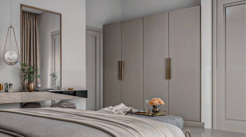 Chambre à coucher moderne aux tons neutres dans Butterfly Towers Arjan, comprenant un grand lit, un bureau flottant avec un miroir au-dessus, une lampe suspendue, des armoires beiges avec de longues poignées, et un petit plateau avec des fleurs sur le lit.