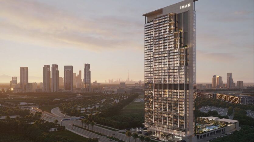 A modern skyscraper bearing the inscription "IMAN" stands at sunset, overlooking the urban landscape. Sierra by IMAN rises above other tall buildings, roads, greenery and an elegant swimming pool in the foreground.