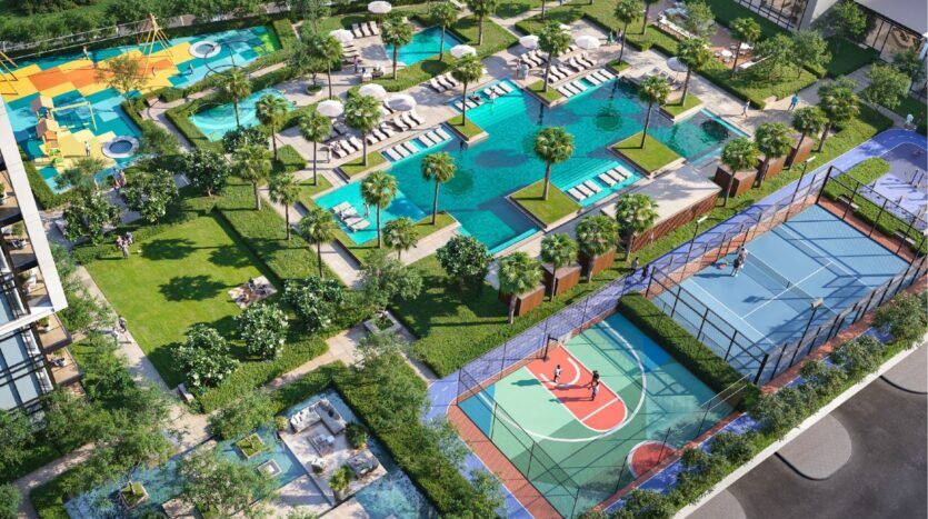 Aerial view of Sierra by Iman's modern outdoor recreation area with pools, sun loungers, palm trees, colorful playground, fenced basketball and tennis courts, all surrounded by landscaped gardens and walking paths.