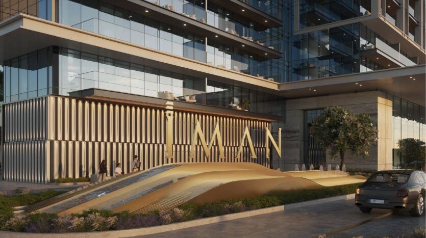 The exterior of a modern building with large glass windows and a gold "IMAN" sign stands out, highlighting the elegance of Sierra by Iman. People stroll by the entrance, while a car is parked nearby on the cobbled driveway.