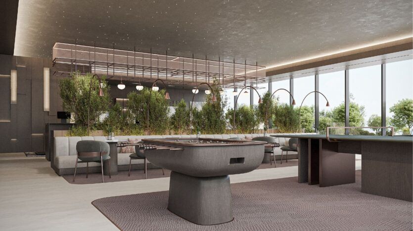 Modern living room featuring sleek furniture by Sierra by Iman, a central foosball table, greenery dividing the seating, large windows offering a view of the outdoors and contemporary lighting fixtures. The open space is elegant and welcoming.