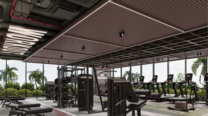 Modern gym with weight machines, treadmills and a "WORKOUT" sign on the ceiling. Large windows reveal palm trees and greenery, creating a bright and welcoming atmosphere at Sierra by Iman.