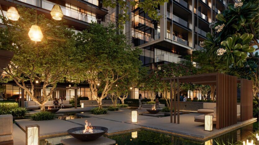 The courtyard of a modern twilight apartment at Sierra by Iman features lush trees, a cozy pergola, bright lanterns, fire pits and a reflective pond, creating a warm and inviting outdoor space.