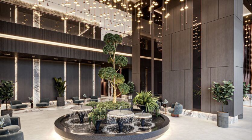 The hotel lobby is modern, with high dark walls, a central circular fountain surrounded by green plants, elegant hanging lamps and stylish armchairs. Discover refined comfort inspired by Sierra by Iman.