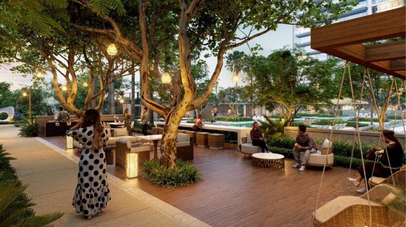 Outdoor lounge with Sierra by Iman furniture, with people relaxing under tall trees and hanging lanterns; a woman in a polka-dot dress strolls along a path, surrounded by lush vegetation.