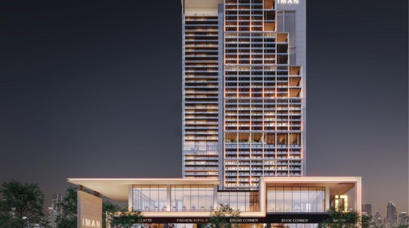 Modern night building with illuminated windows; the lower part features commercial spaces labeled "LATTE", "FASHION AVENUE", "BREAD CORNER" and "BOOK CORNER". The building is branded "IMAN" and belongs to Sierra by IMAN.