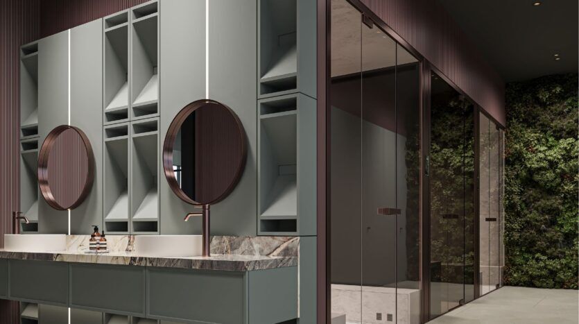 Modern bathroom with two round mirrors above a marble countertop, light gray cabinetry, rose gold fixtures and a glass shower. A green vertical garden decorates the wall outside the shower, with touches inspired by Sierra by Iman.
