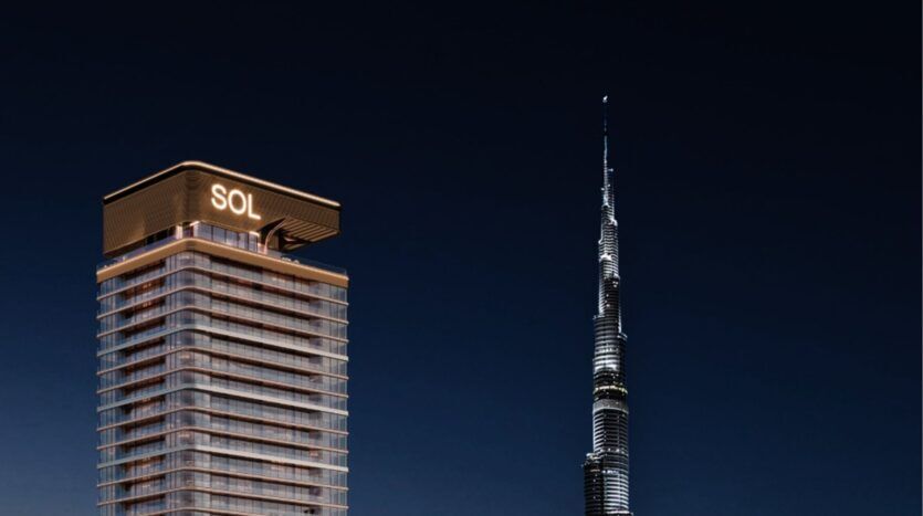 Une tour moderne, la Sol Luxe Tower, est illuminée la nuit et se dresse à côté de la Burj Khalifa, plus haute et semblable à une aiguille, dans un ciel sombre.