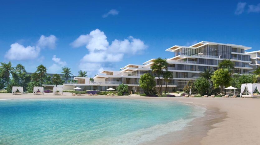 Palm Central, a modern beachfront resort, features multi-storey white buildings, palm trees, sun loungers and cabanas along a sandy shoreline. The turquoise ocean is calm under a bright blue sky dotted with clouds.