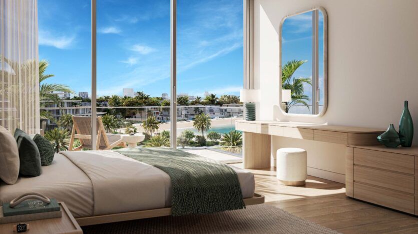 The modern Palm Central room features large windows overlooking palm trees and the pool. The bed has green accents, complemented by a wooden vanity, mirror, glass vases and natural light streaming across the wooden floors.