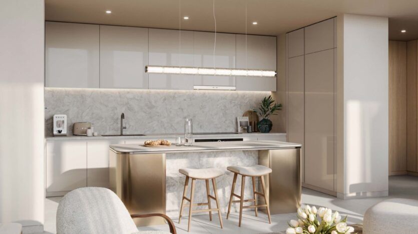 Modern kitchen at Palm Central with white cabinets, marble backsplash and matching island with two wooden stools. A linear pendant lamp hangs over the island, while decorative objects and appliances are neatly arranged on the countertops.