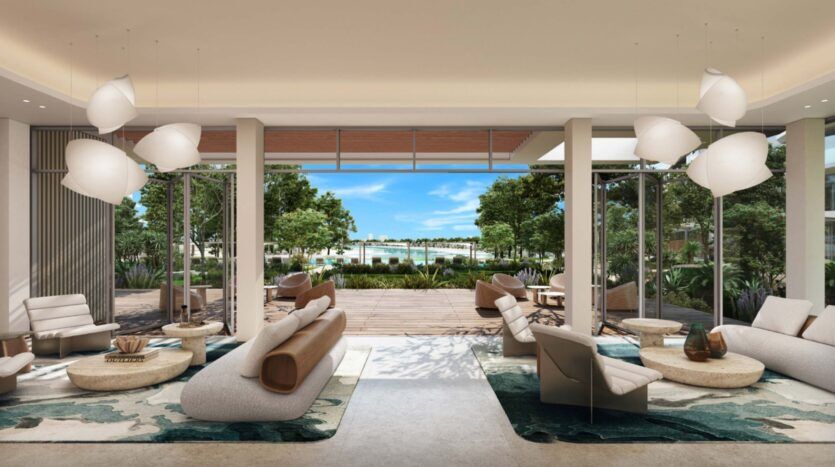 Modern, elegant Palm Central living room with neutral furnishings, round coffee tables and artistic lighting. Floor-to-ceiling windows open onto a wooden terrace, lush greenery and a pool with palm trees under a brilliant blue sky.