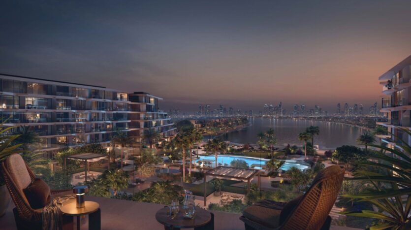 At dusk, the luxurious Palm Central balcony overlooks modern apartments, illuminated pools, palm trees and the distant city skyline, creating an elegant, serene atmosphere.