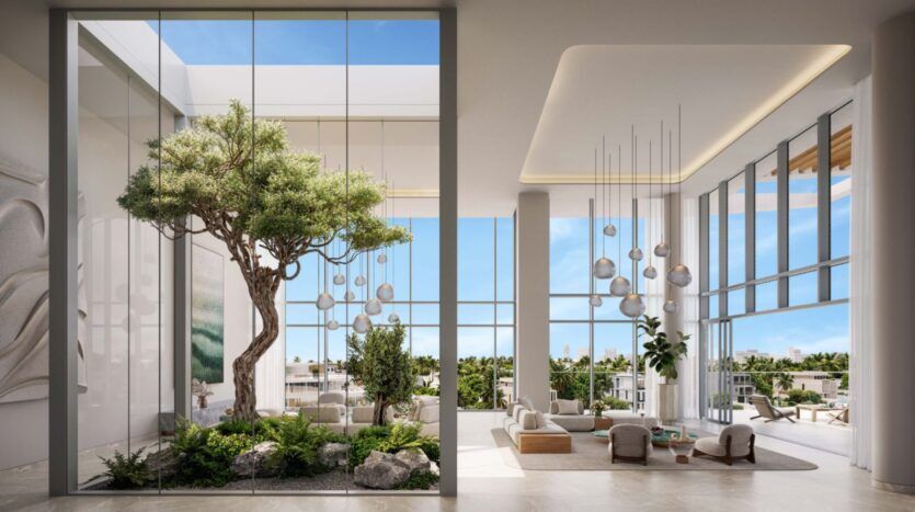 The modern, spacious Palm Central lounge features floor-to-ceiling windows, indoor plants, minimalist furniture and an indoor garden with a large tree, creating a bright, airy atmosphere filled with natural light and greenery.