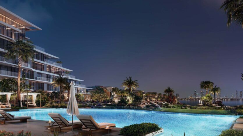 A luxurious night pool in Palm Central, surrounded by sun loungers, parasols, palm trees and modern buildings, with city lights twinkling in the background under a clear sky.