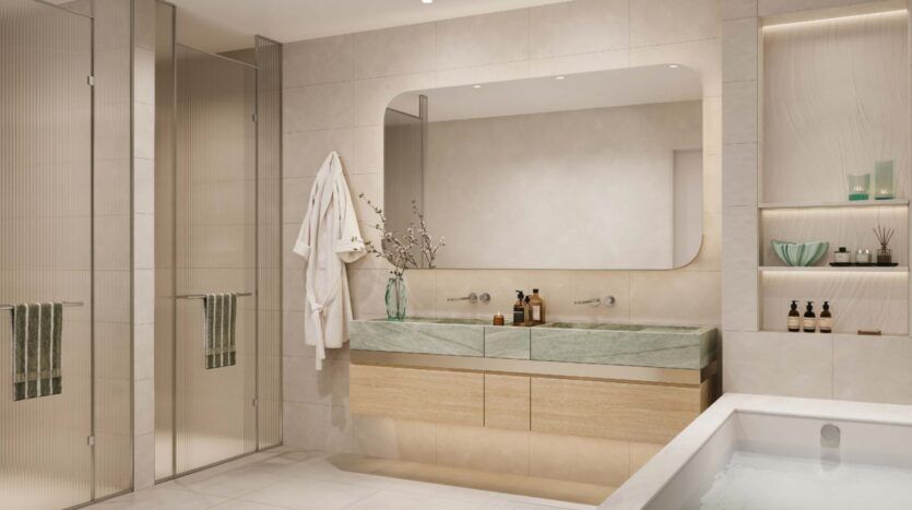 Modern bathroom at Palm Central with a large mirror, two sinks with green countertops, wooden cabinets, glass shower, white bathtub, open shelves with decorations, and a white bathrobe hanging on the wall.