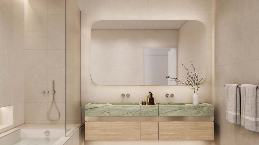 Modern bathroom at Palm Central with beige tiles, green marble double vanity unit, large rectangular mirror, vase with branches and two towels on the wall. The bathtub and shower are visible on the left.