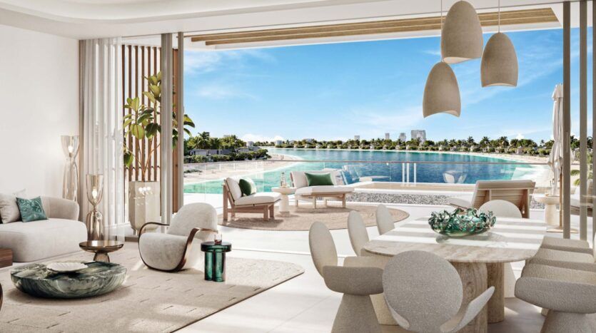 The Palm Central's luxurious modern living and dining room opens onto a terrace with sun loungers, overlooking a tranquil pool and palm trees under a brilliant blue sky. Neutral tones and elegant decor create a serene, welcoming atmosphere.