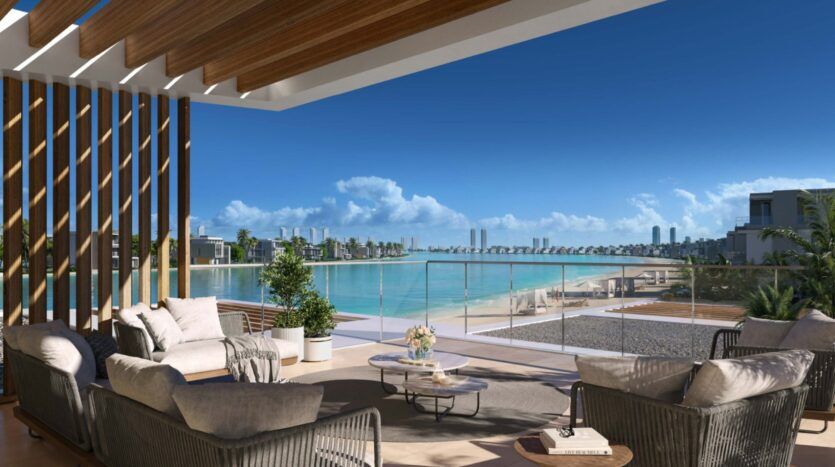 Modern outdoor terrace at Palm Central with comfortable seating and low tables overlooking a tranquil lagoon, sandy beach and distant city skyline under a clear blue sky.