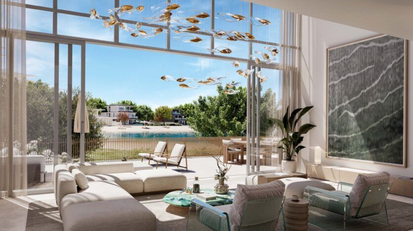 Modern living room at Palm Central with large windows overlooking a garden and pool, with light-colored furniture, a glass coffee table, a large plant and a sculptural light fixture. The atmosphere is bright and airy.