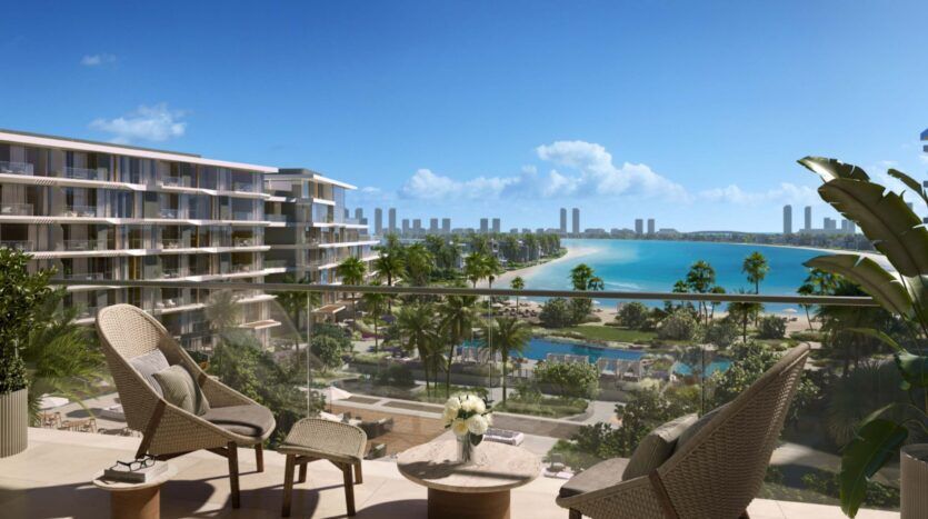 A modern balcony at Palm Central with wicker chairs and a small table overlooks a resort, palm trees, pool and turquoise water with the city skyline and skyscrapers in the background under a blue sky.
