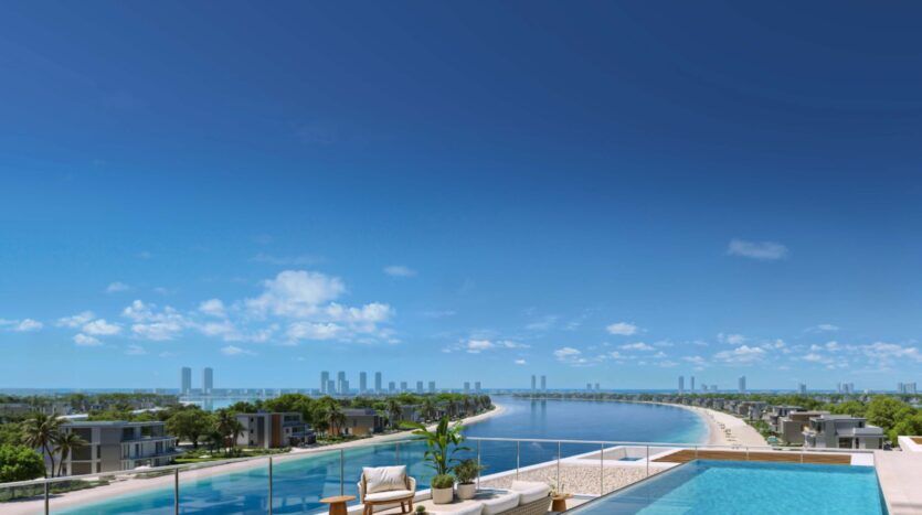 A rooftop pool and sun loungers overlook a calm, blue waterway in Palm Central, with modern villas, palm trees and a distant skyline under clear, sunny skies.
