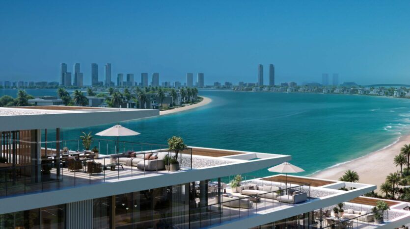 Palm Central's modern beachfront apartments feature spacious terraces overlooking a turquoise bay, sandy beach and palm trees. Skyscrapers soar over the distant city skyline under a clear blue sky, creating a luxurious, serene coastal scene.