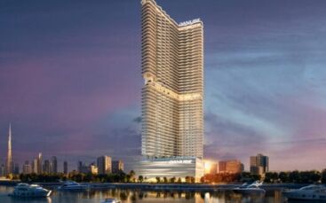 Un gratte-ciel moderne et illuminé portant le nom de "Danube" se dresse près du front de mer au crépuscule dans la ville maritime ; des yachts et des bateaux glissent sur l'eau tandis que les gratte-ciel créent une ligne d'horizon animée.
