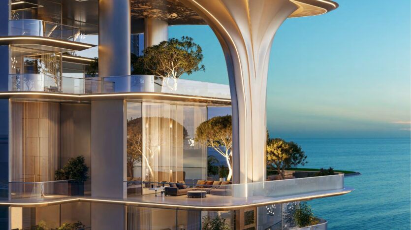 L'immeuble de luxe moderne Breez by Danube Maritime City, avec ses grandes baies vitrées, ses terrasses spacieuses et sa verdure, donne sur une mer calme et bleue au coucher du soleil. L'architecture se caractérise par des lignes douces et courbes et des arbres intégrés dans le design.