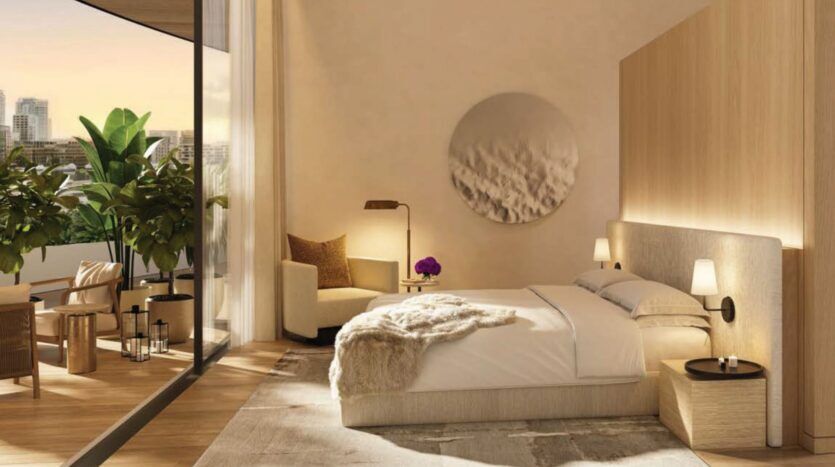 Une chambre moderne à The Edition avec un grand lit, un décor neutre et un éclairage doux. Des fenêtres allant du sol au plafond s'ouvrent sur un balcon offrant une vue sur la ville et des plantes luxuriantes. Un fauteuil confortable, des tables d'appoint et des œuvres d'art murales complètent cet espace serein.