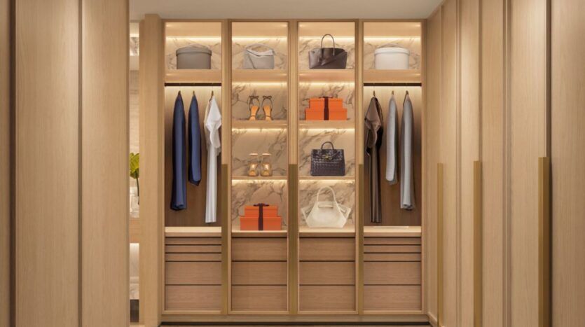Le dressing moderne de The Edition comporte des étagères en bois clair, des tiroirs et des touches de marbre rétroéclairées. Les vêtements, les sacs à main, les chaussures et les boîtes orange caractéristiques y sont soigneusement suspendus, ce qui donne un aspect propre, organisé et luxueux à l'ensemble.