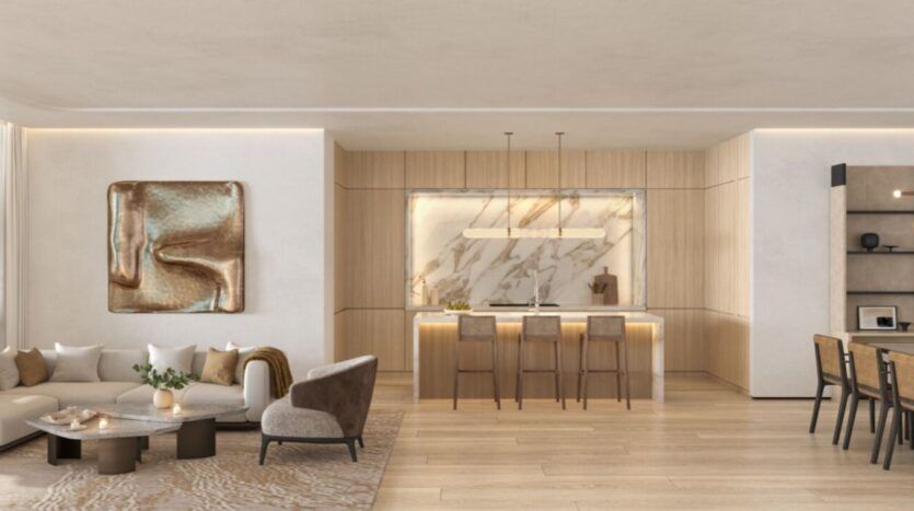 L'espace de vie moderne et ouvert de l'hôtel The Edition comprend un canapé sectionnel beige, des œuvres d'art murales abstraites, un îlot de cuisine en marbre avec des tabourets de bar et un coin repas, le tout accentué par des finitions en bois clair et des tons neutres.