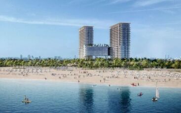 Une grande plage de sable à Soto Grande avec des gens qui se promènent et se détendent près de l'eau, bordée de palmiers. À l'arrière-plan, deux grands bâtiments modernes avec une structure de liaison se détachent sur le ciel bleu, tandis que de petits bateaux et des kayaks sillonnent l'eau.