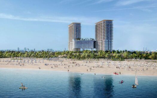 Una grande spiaggia sabbiosa a Soto Grande con persone che passeggiano e si rilassano vicino all'acqua, circondata da palme. Sullo sfondo, due grandi edifici moderni con una struttura di collegamento si stagliano contro il cielo blu, mentre piccole barche e kayak solcano l'acqua.