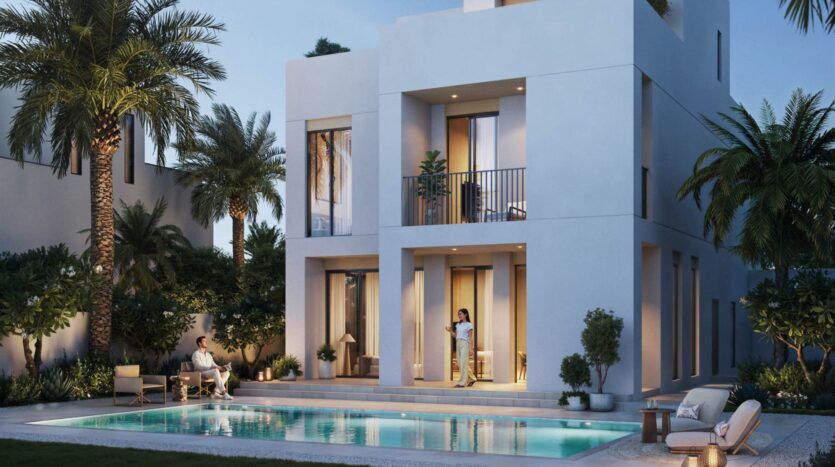 Une maison blanche moderne de deux étages à The Heights, avec de grandes fenêtres, entourée de palmiers et de jardins. Une piscine se trouve au premier plan ; une femme se tient sur le patio et un homme est assis à proximité, profitant d'une soirée paisible en plein air.