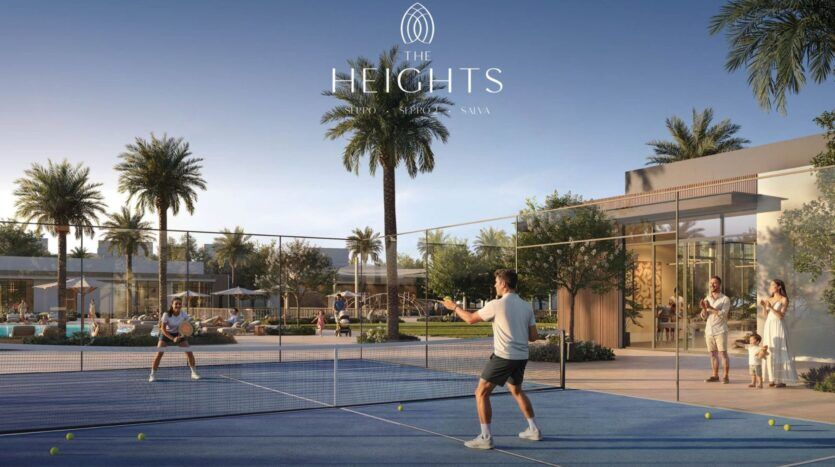 Deux personnes jouent au tennis sur un court extérieur à The Heights, entouré de palmiers et de bâtiments modernes, tandis qu'une famille surveille les alentours dans cette luxueuse communauté résidentielle.