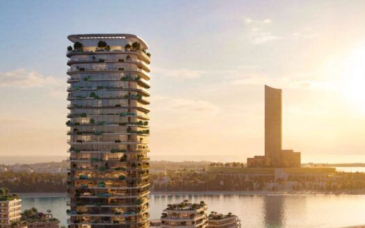 Una torre moderna, Le Château, con balconi ricurvi e vegetazione lussureggiante, si erge sul bordo dell'acqua al tramonto, mentre un'altra grande torre si staglia sullo sfondo sopra le acque calme che riflettono il calore del cielo.