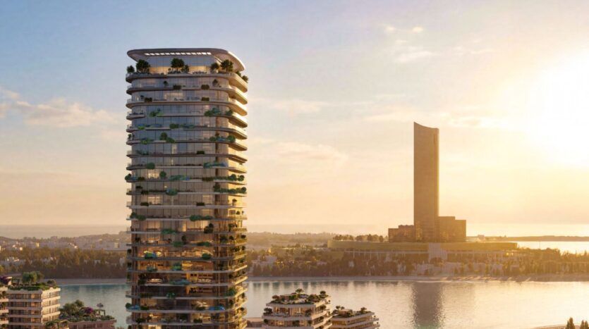 A modern tower, Le Château, with curved balconies and lush vegetation, stands at the water's edge at sunset, while another large tower rises in the background above the calm waters reflecting the warmth of the sky.