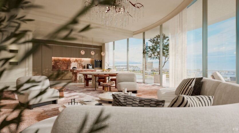 The modern, sun-filled living room, with its curved floor-to-ceiling windows, neutral-toned sofas, and round coffee table, evokes the elegance of the Château. It is complemented by a stylish open kitchen with a marble island and pendant lights.