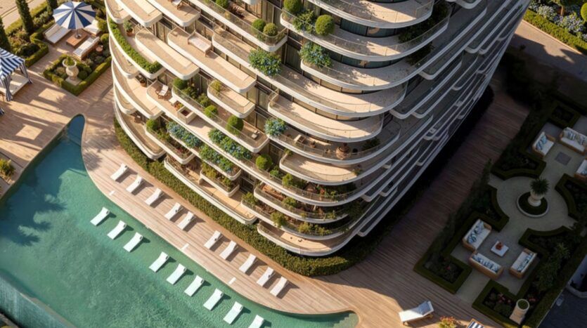 Aerial view of the Château, a modern tower with curved balconies, lush vegetation, and a large outdoor pool with lounge chairs and landscaped gardens below.