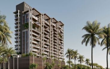 Un immeuble moderne de plusieurs étages avec de grands balcons et des façades en verre se dresse à Sea Cliff, entouré de grands palmiers sous un ciel bleu limpide.