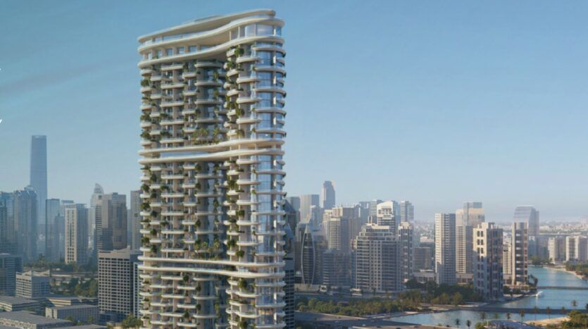 Amali Residences est un immeuble moderne de grande hauteur avec des balcons incurvés et de la verdure, qui se dresse dans l'horizon de la ville, entouré d'autres grands immeubles et d'une rivière sous un ciel bleu limpide.