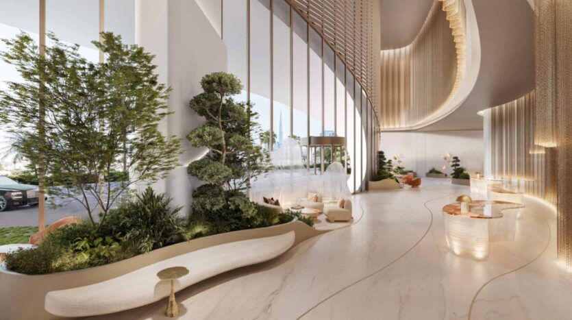 Le hall de l'hôtel Amali Residences est moderne et aéré, avec de hautes fenêtres, des accents dorés incurvés, de la verdure à l'intérieur, des sols en marbre clair, des sièges confortables et un éclairage naturel doux. Une voiture et des arbres en plein air sont visibles à travers les fenêtres.