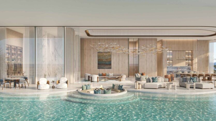 Luxueux espace de vie ouvert dans les résidences Amali, avec des sièges élégants, une décoration moderne et de grandes parois vitrées donnant sur une piscine à débordement qui se prolonge dans la pièce, créant ainsi un espace intérieur-extérieur homogène.