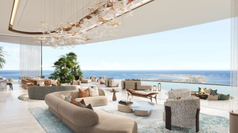 Le salon luxueux et moderne des résidences Amali comprend des canapés incurvés et de grandes fenêtres offrant une vue panoramique sur l'océan. Le décor élégant comprend des plantes, des éclairages uniques et des meubles aux tons neutres, créant une atmosphère aérée et relaxante.