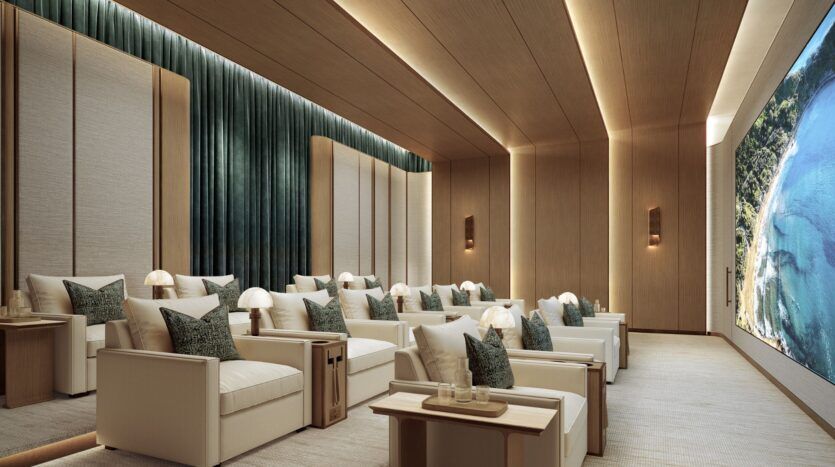 La luxueuse salle de cinéma du Four Seasons Private Residences est équipée de fauteuils blancs, de tables d'appoint avec lampes, de rideaux verts, de murs et de plafonds en bois et d'un grand écran affichant une vue pittoresque de la côte.