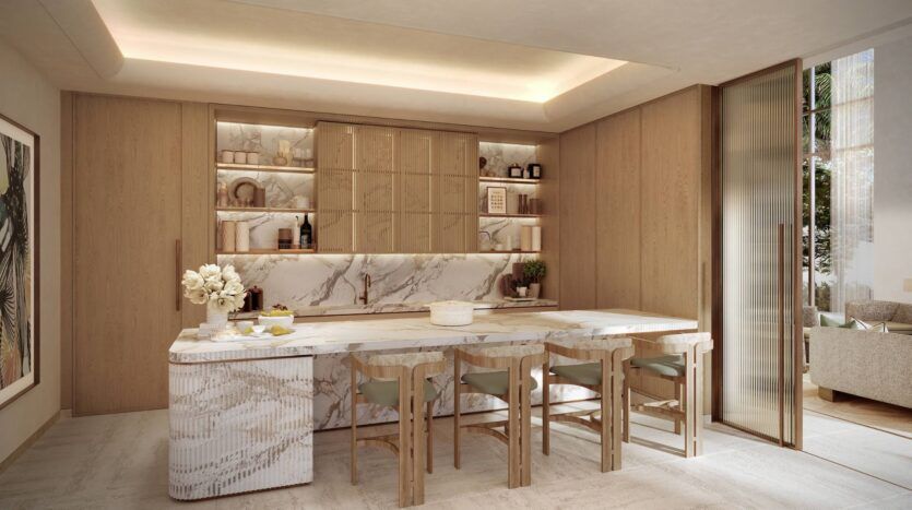 La cuisine moderne de Four Seasons Private Residences se compose d'armoires en bois clair, d'étagères ouvertes, d'un îlot en marbre avec quatre chaises en bois et d'un éclairage intégré. Des objets décoratifs et des fleurs créent une atmosphère propre et accueillante.