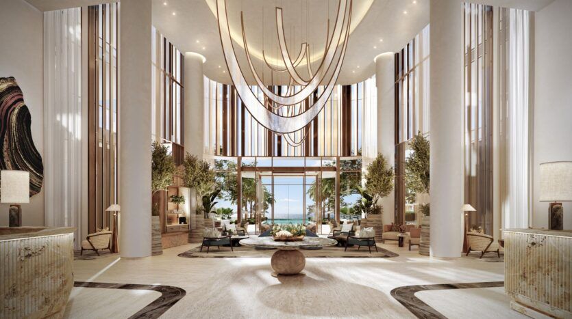 Le luxueux hall d'entrée de l'hôtel Four Seasons Private Residences présente de hauts plafonds, des luminaires modernes suspendus, de hautes colonnes, de grandes fenêtres avec des accents en bois, des plantes d'intérieur, d'élégants sièges et une vue imprenable sur l'océan.